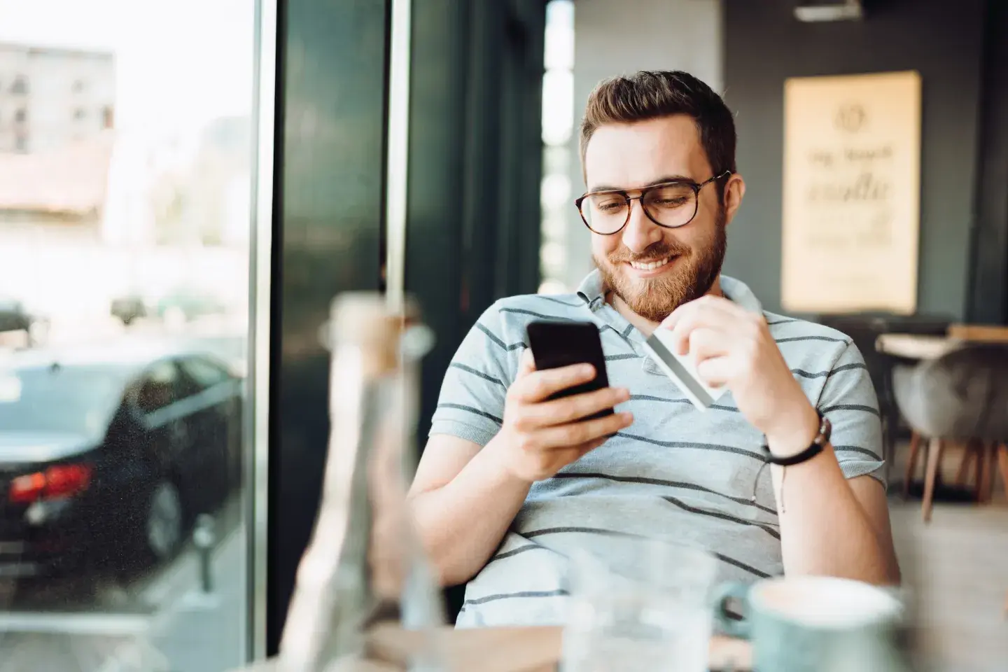Man in coffee shop on phone with credit card