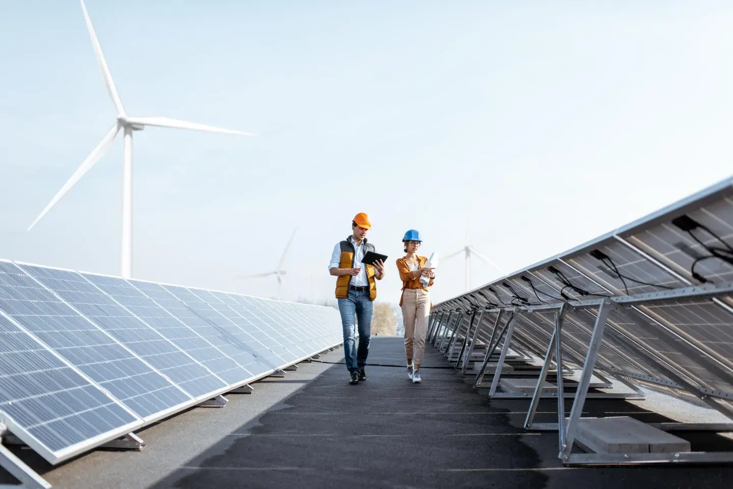 two people walking next to solar panels and wind turbines