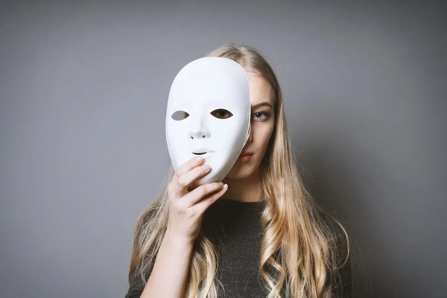 Young blonde woman with white mask over half of her face on gray background